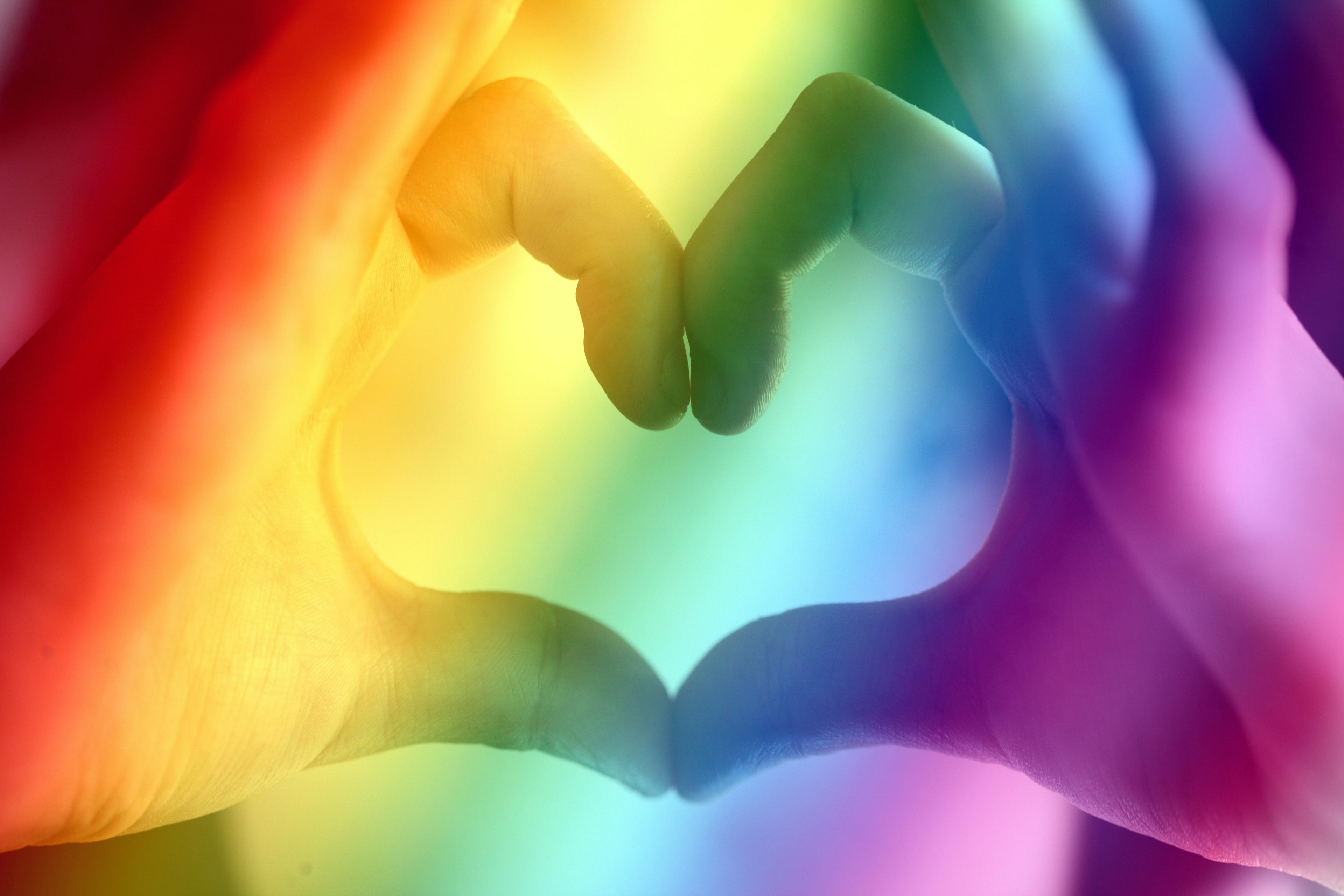 Two hands forming a heart shape against a rainbow-colored background